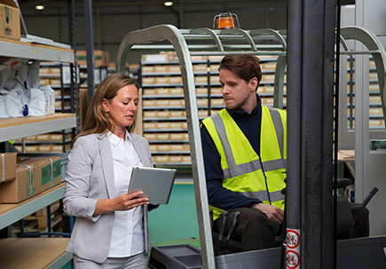 Man and woman in warehouse looking over a tablet. Man and woman in warehouse looking over a tablet.