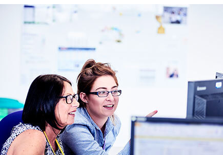 Women working together in front of computer monitors. Women working together in front of computer monitors.